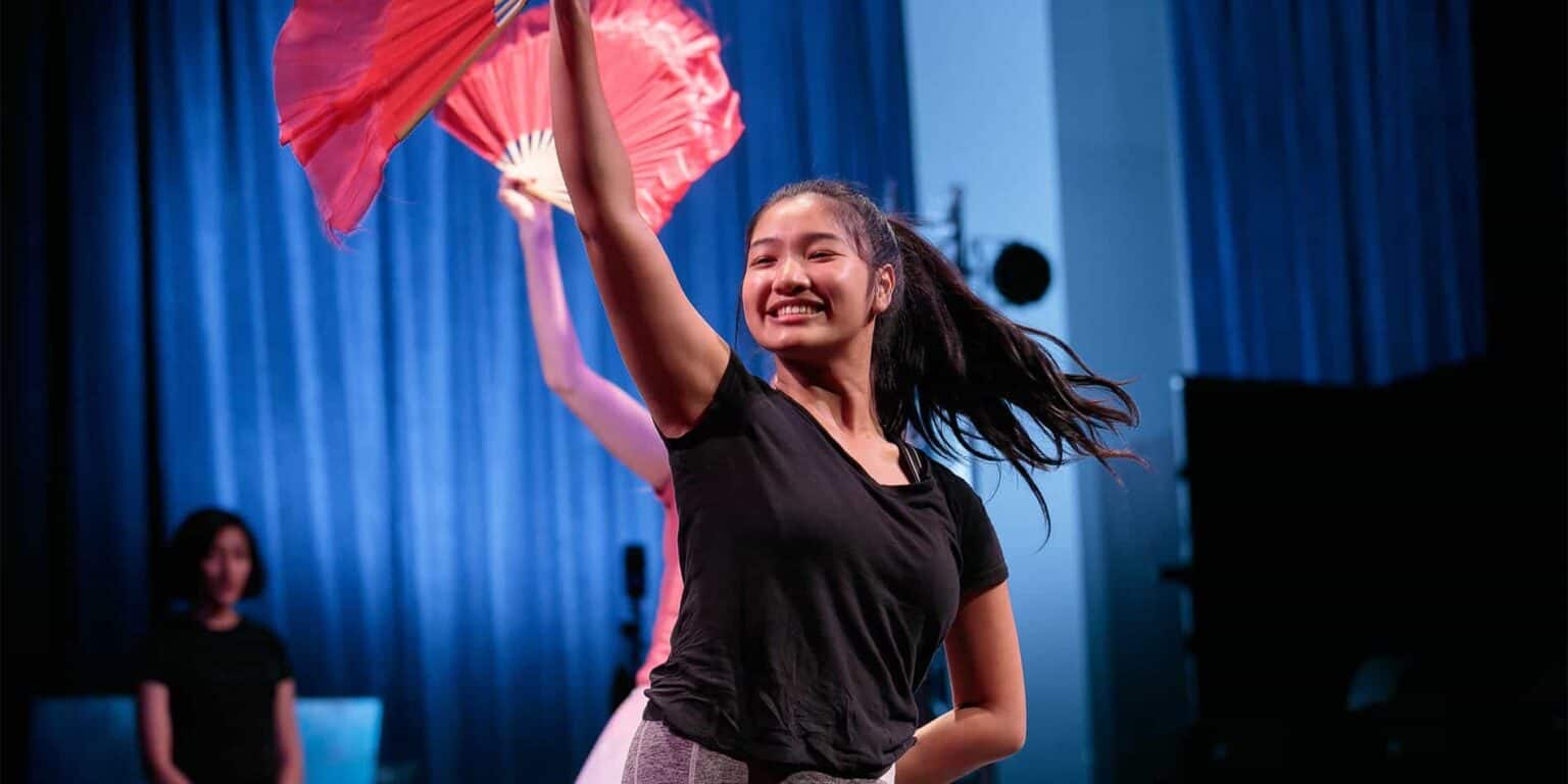 Lively young girl smiling during performance with fans on stage at World Schools event.