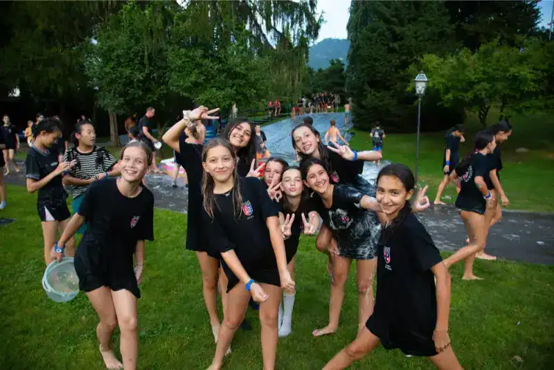 This Month at TASIS: June 2024 27 Children enjoying water activities at a World Schools camp in lush green outdoor setting.