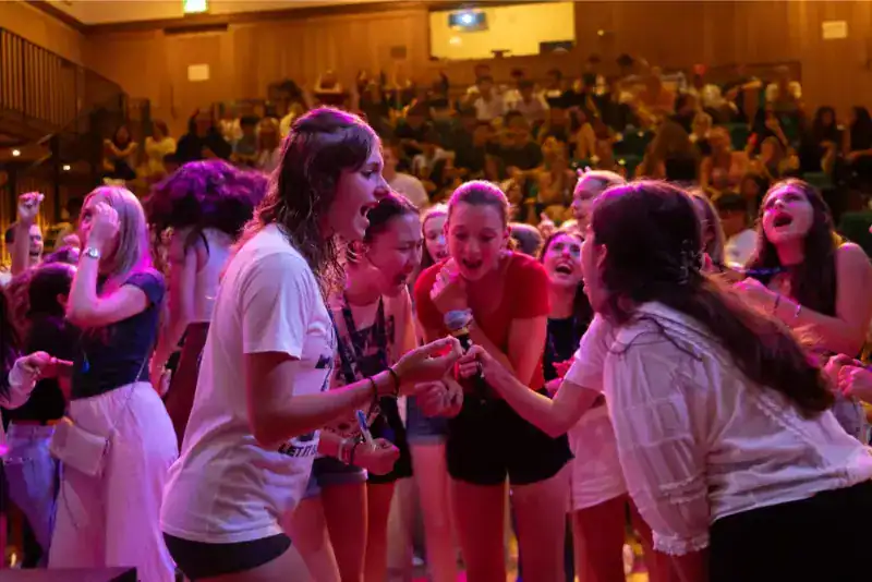 This Month at TASIS: June 2024 28 Excited children performing on stage at World Schools event with vibrant energy and joyful expressions.