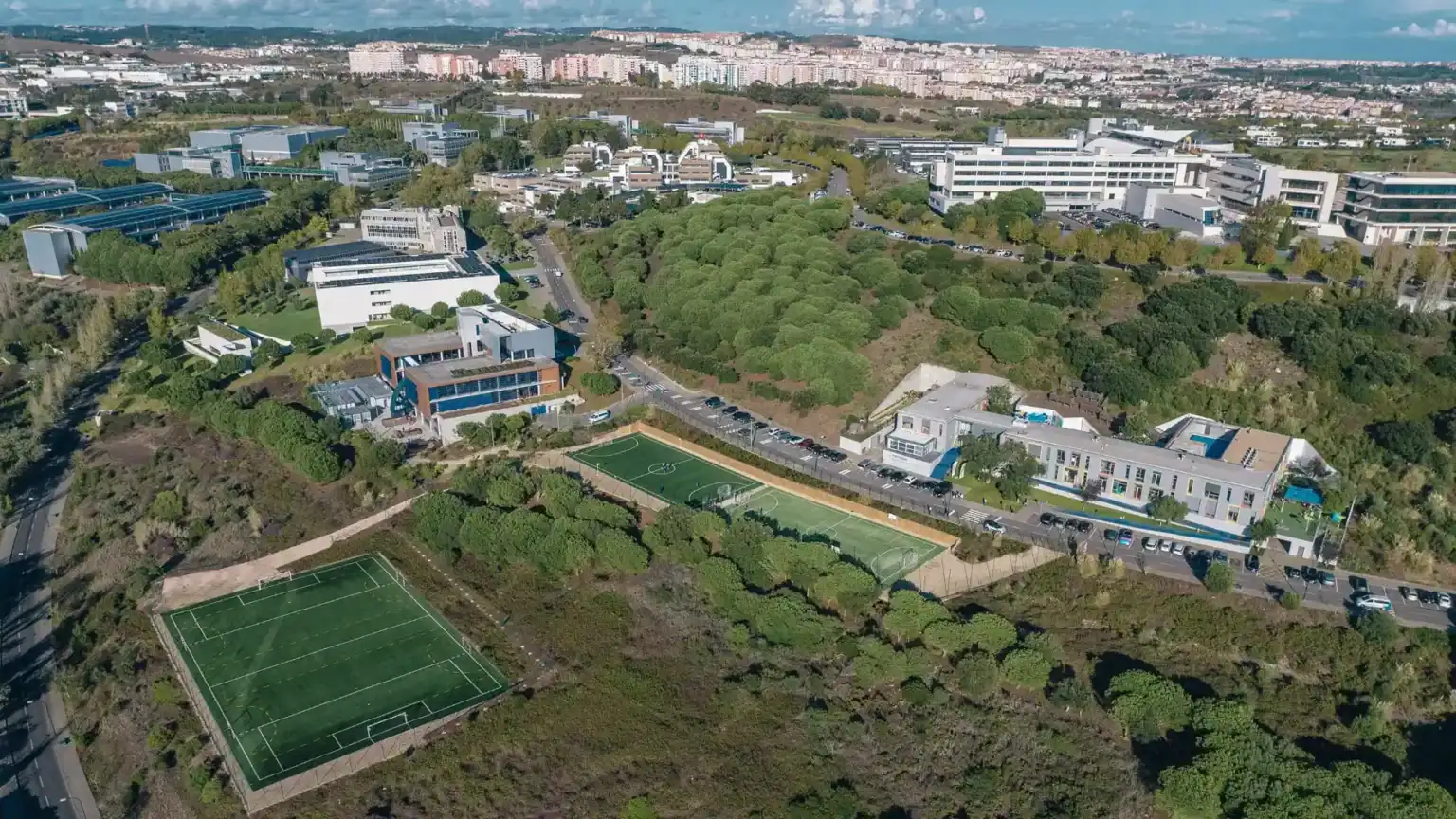 Modern international school campus with sports facilities and green areas, located in an urban setting.