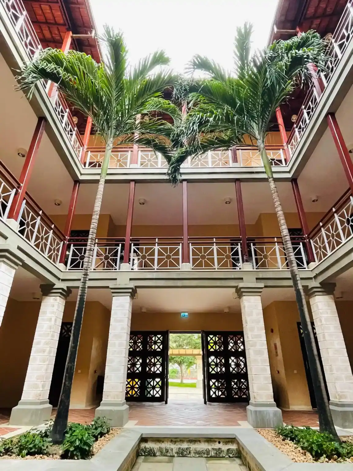 فناء داخلي نابض بالحياة مع أشجار النخيل الوارفة والضوء الطبيعي والهندسة المعمارية الأنيقة في حرم مدرسي عالمي المستوى.