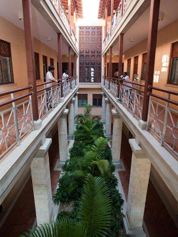 المساحات الخضراء الداخلية المورقة في ردهة المدرسة الحديثة ذات الشرفات المفتوحة والطلاب الذين يدرسون.