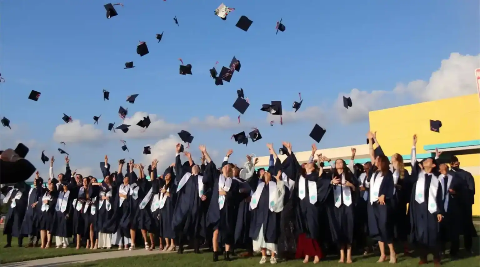 Graduates celebrating graduation ceremony at World Schools, throwing caps in the sky.