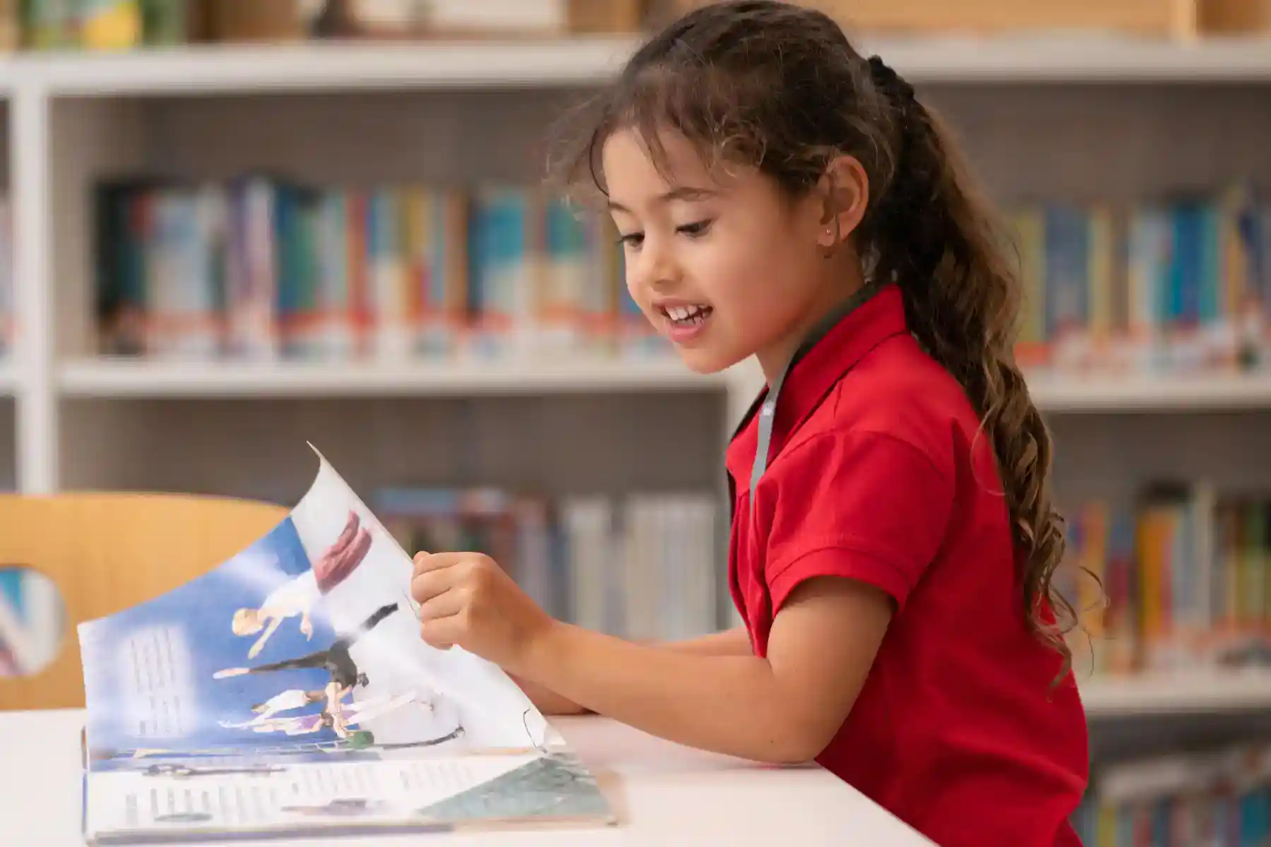 Bright young girl reading an educational magazine in a school library, promoting academic excellence and student engagement.