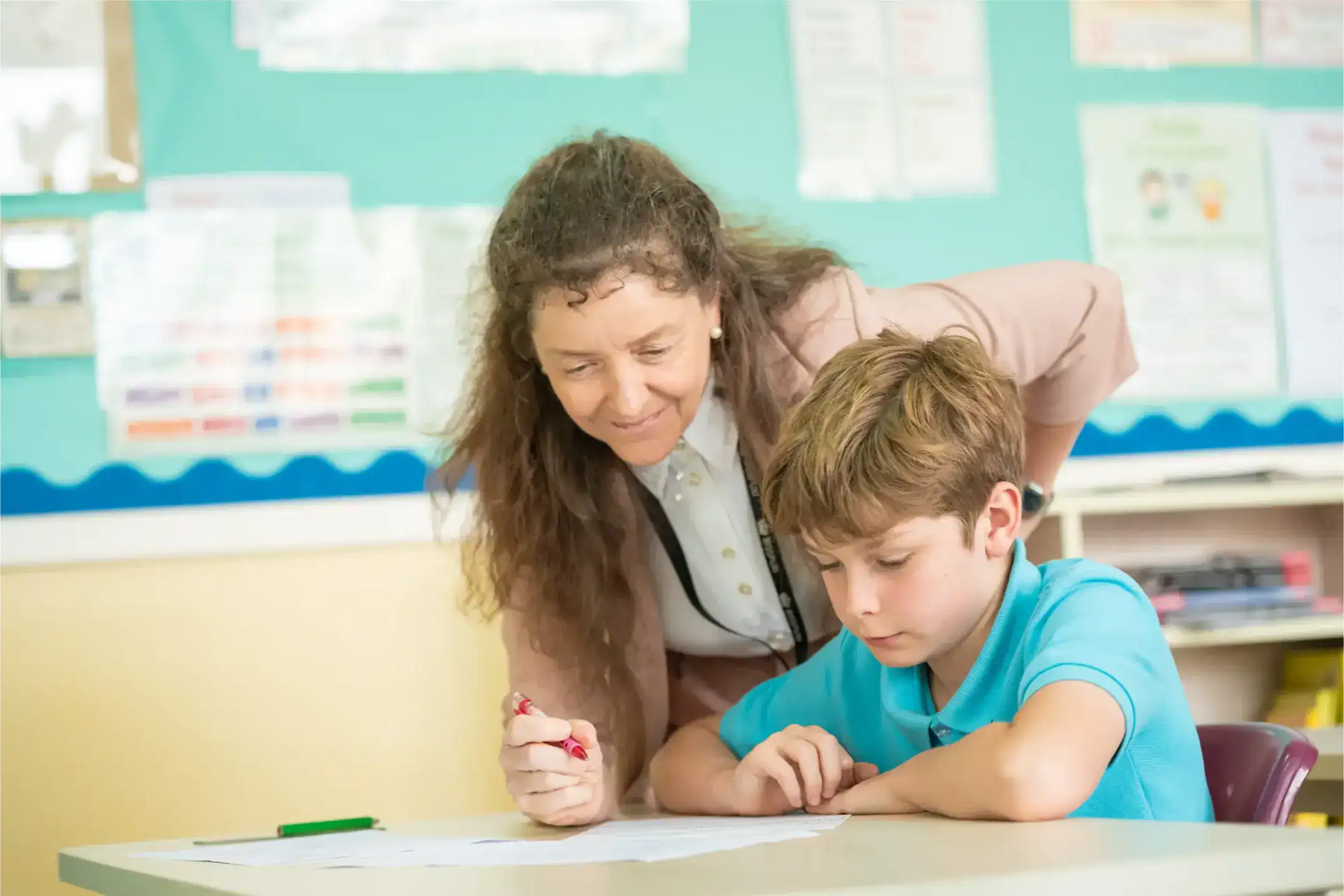 Focused teacher assisting young student with classroom activity, emphasizing educational support and learning.