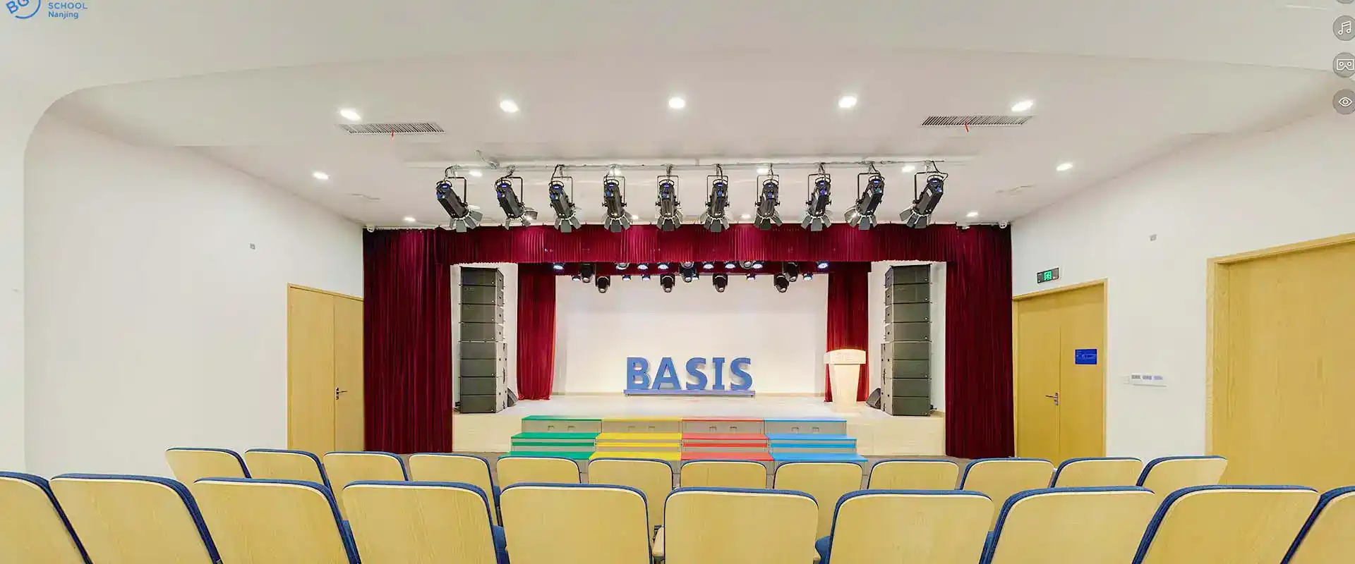 Bright school auditorium with stage, red curtains, and seating for students, ideal for visual and performing arts education.
