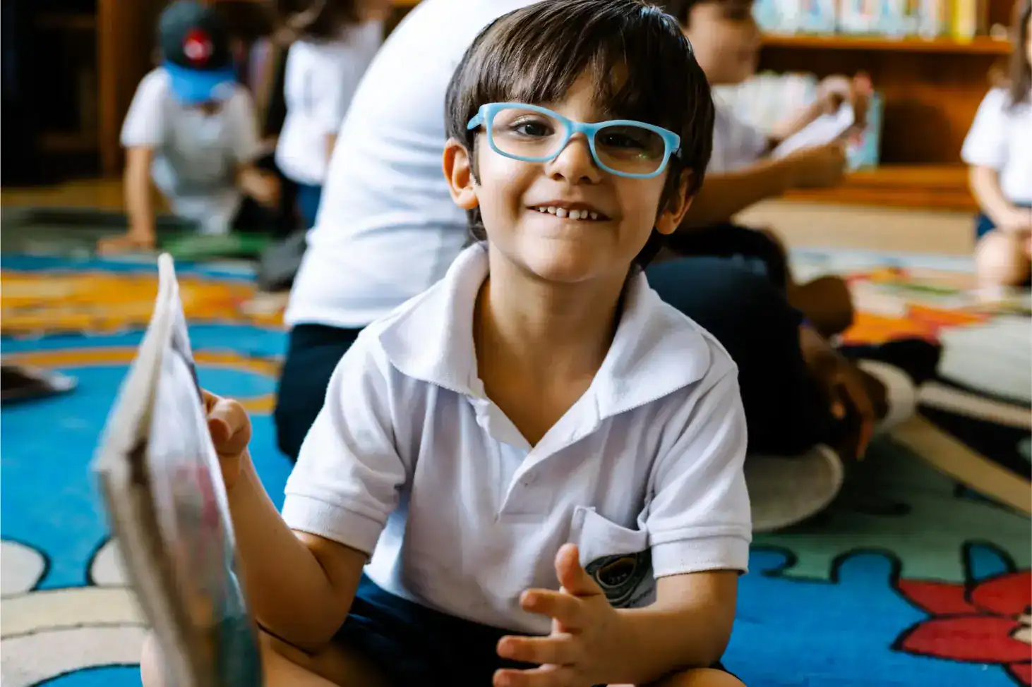 Bright young boy with glasses smiling in classroom at a World Schools educational event.