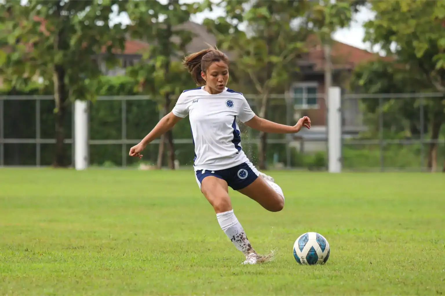 Joven jugadora de fútbol en acción durante un partido en el frondoso campo de la escuela.