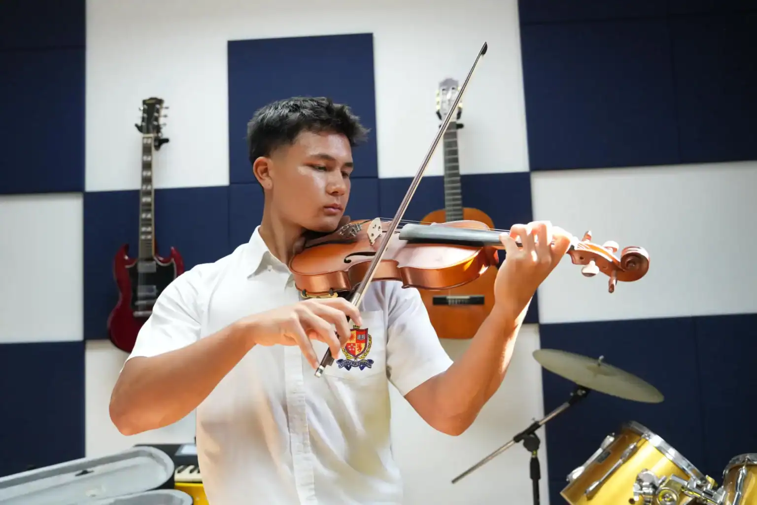 Joven estudiante tocando el violín en el aula de música con guitarras y tambores de fondo.