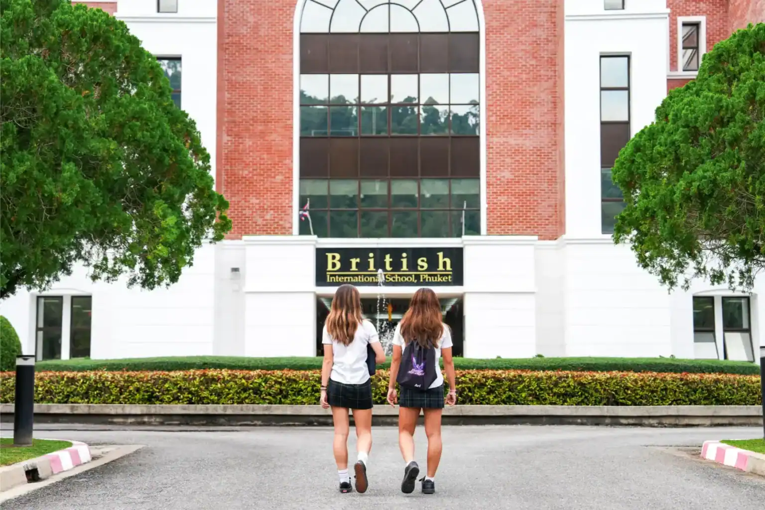 Alumnos caminando hacia British International School Phuket en uniforme, que ofrece una educación de calidad y un plan de estudios internacional.
