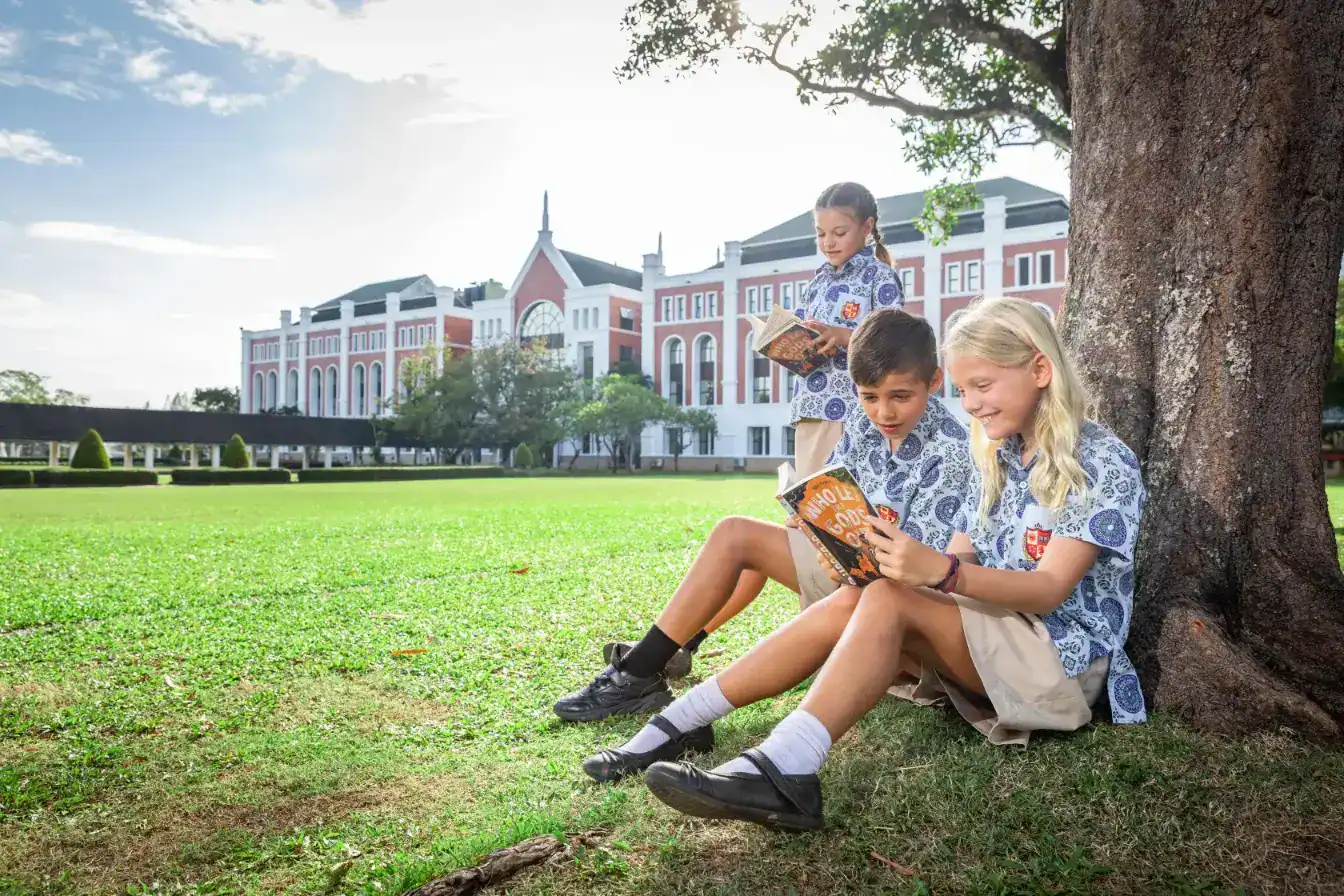 Alumnos leyendo libros al aire libre en el campus de un prestigioso colegio internacional a la luz del sol, entorno educativo, aprendizaje al aire libre, campus escolar, vida en el campus.