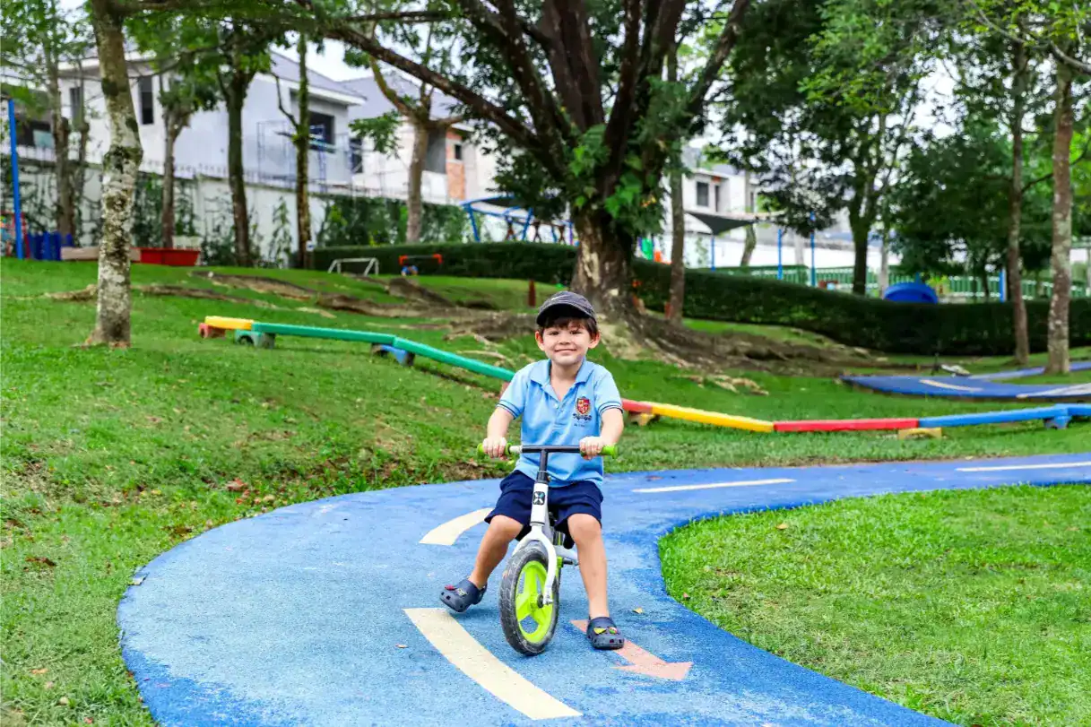 Niño montando en bicicleta de equilibrio en un colorido parque infantil al aire libre en un campus de los Colegios del Mundo.