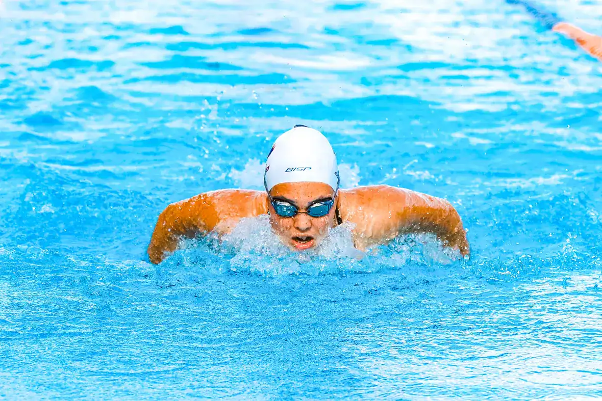 Nadador de competición realizando brazada de mariposa en piscina azul, mostrando entrenamiento de deportes acuáticos de élite.