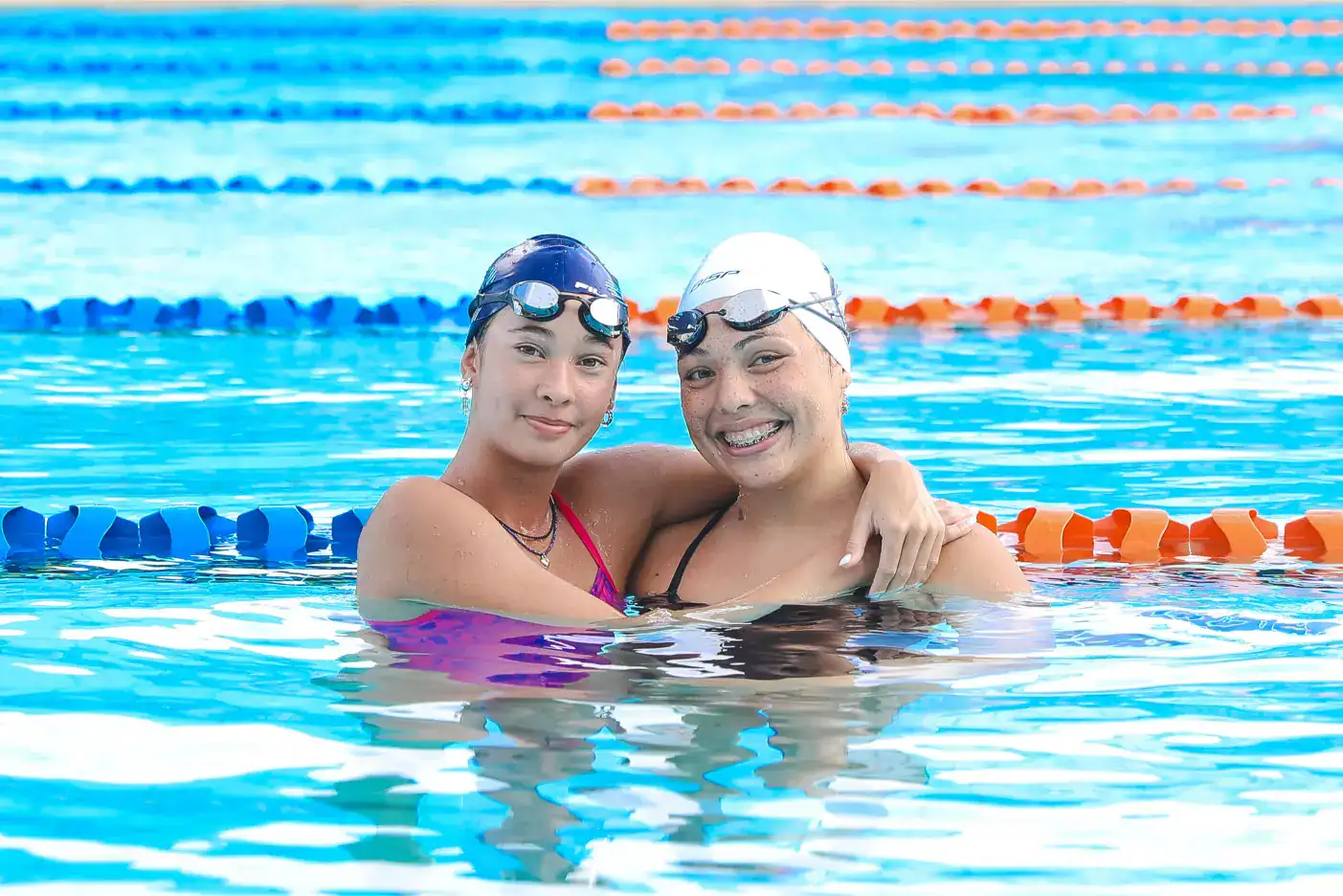 1. Dos nadadoras en la piscina con gafas, sonriendo, abrazadas.