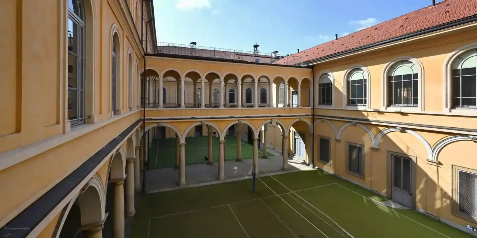 Beautiful historic school courtyard with yellow arches and a sports field, promoting academics and extracurricular development.