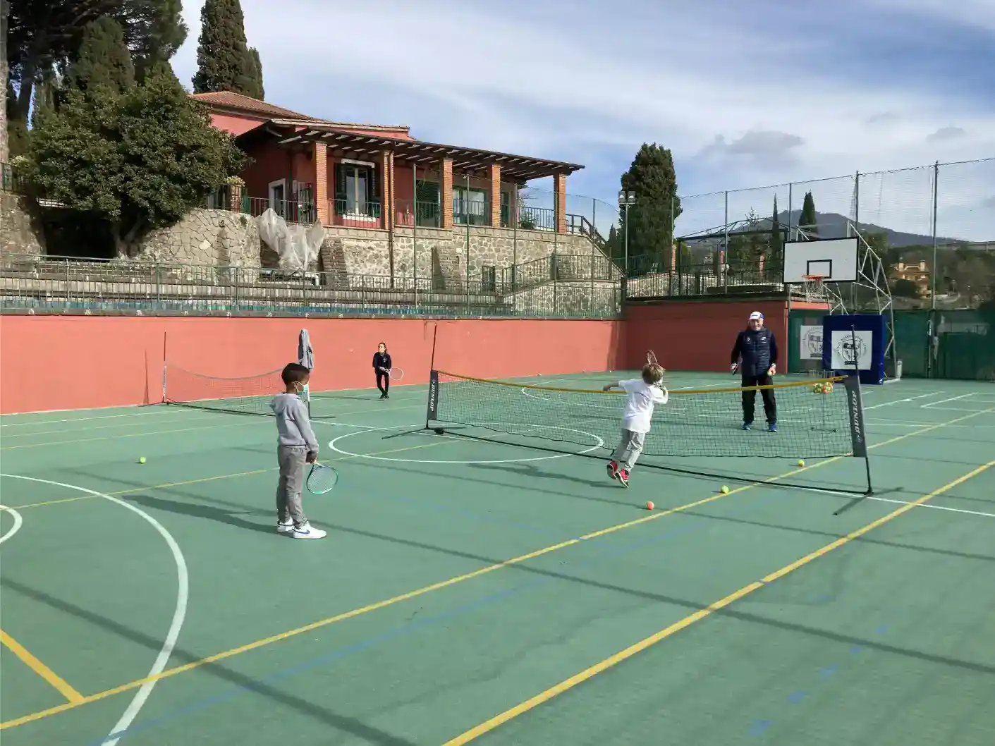 Children playing tennis on an outdoor sports court at a World Schools facility.