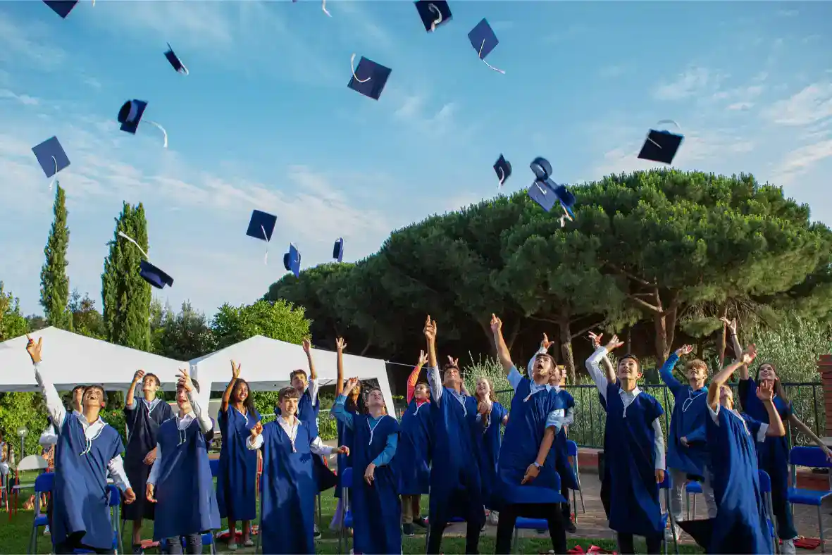 Graduates celebrating outdoors after graduation ceremony at traditional world school.