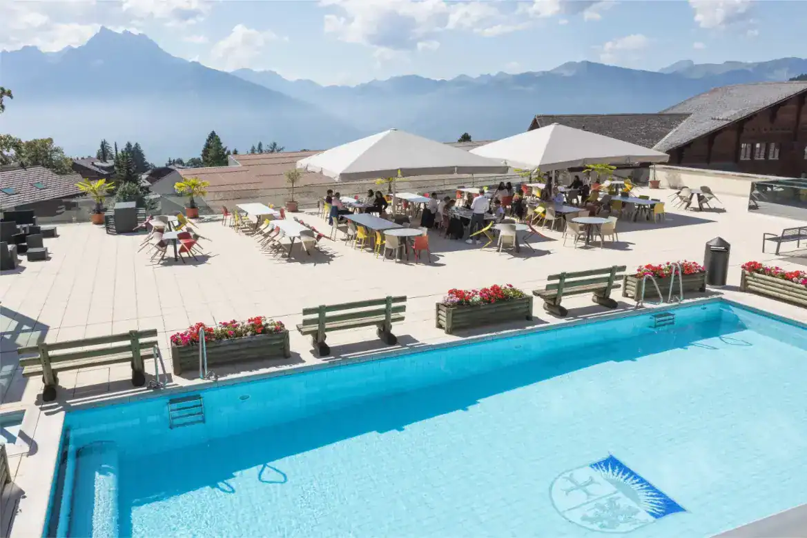Modern school rooftop terrace with swimming pool and outdoor seating in scenic mountain view setting.