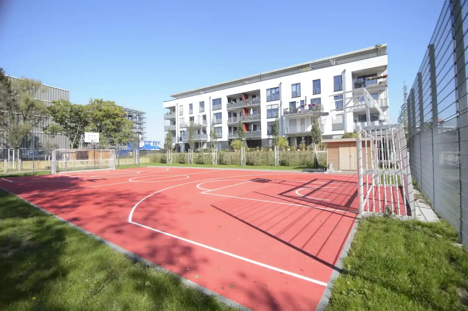 Bright outdoor basketball court at a modern World Schools campus with residential buildings and clear blue sky.