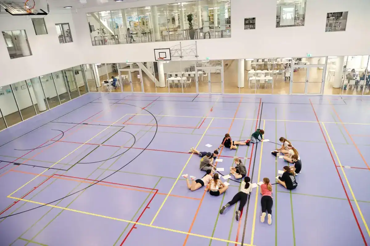 明るい近代的な学校の体育館では、生徒たちがグループ・プロジェクトに取り組んでおり、世界のトップ校の革新的な学習が紹介されている。.