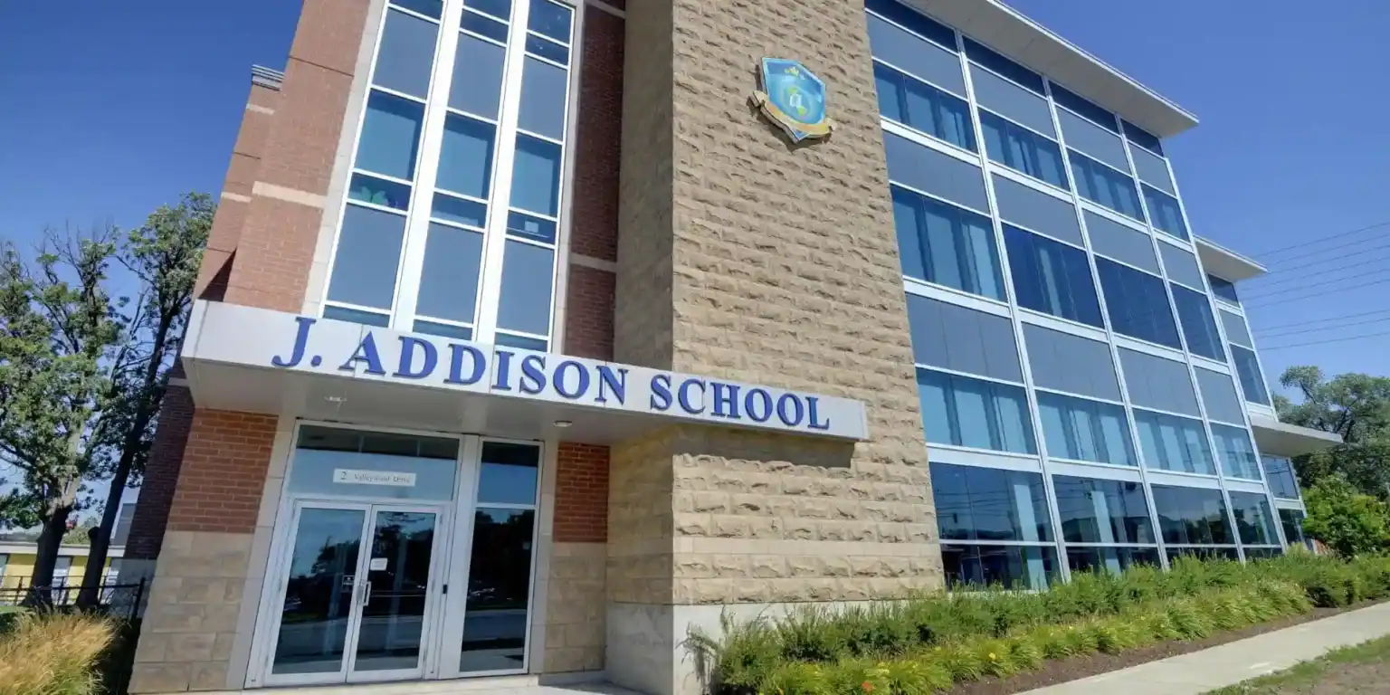 Edifício de ensino moderno na J. Addison School com grandes janelas de vidro e uma envolvente ajardinada.