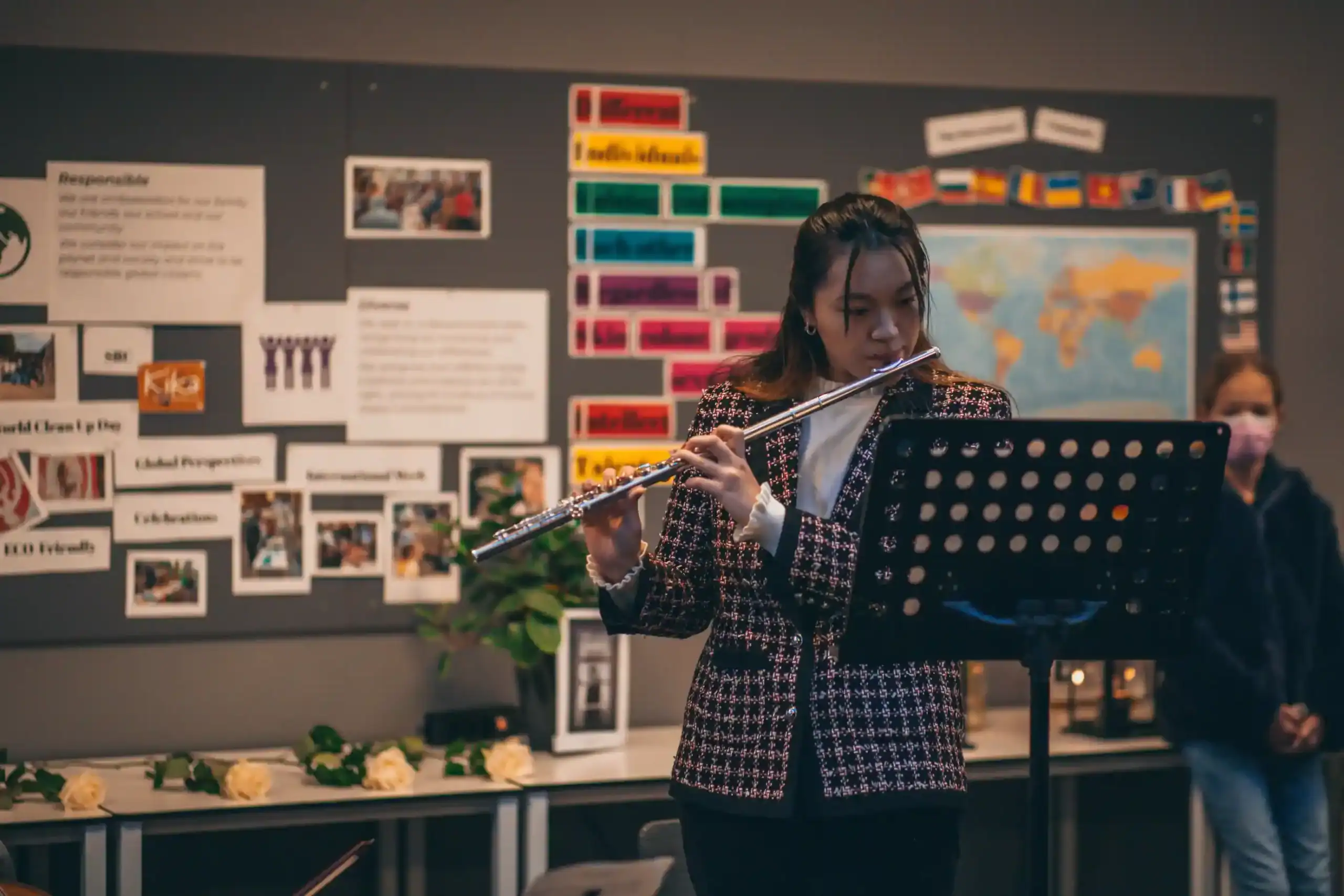 Young girl playing flute in classroom with world map and educational posters.