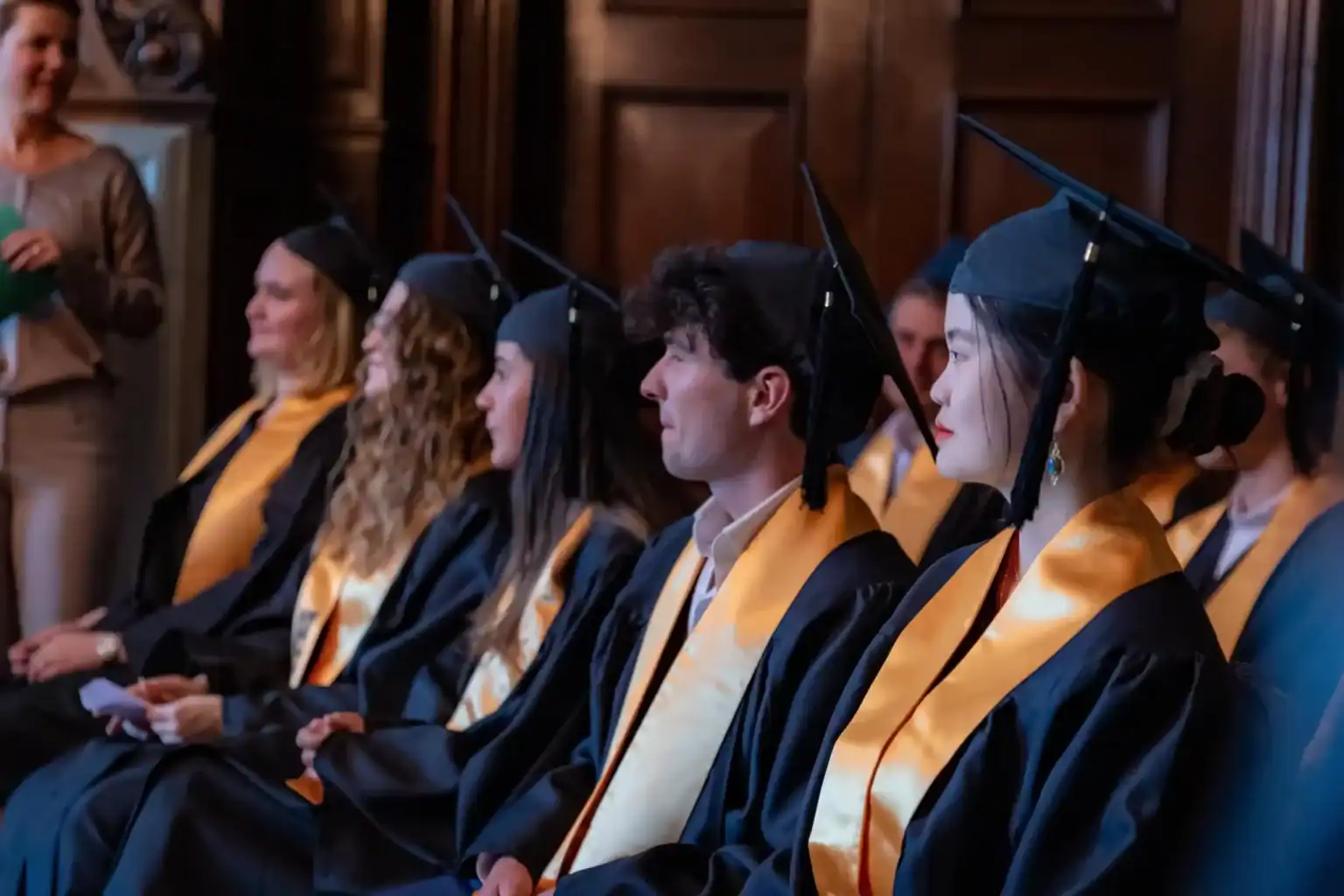 Graduate students wearing caps and gowns at a graduation ceremony, celebrating academic achievement.