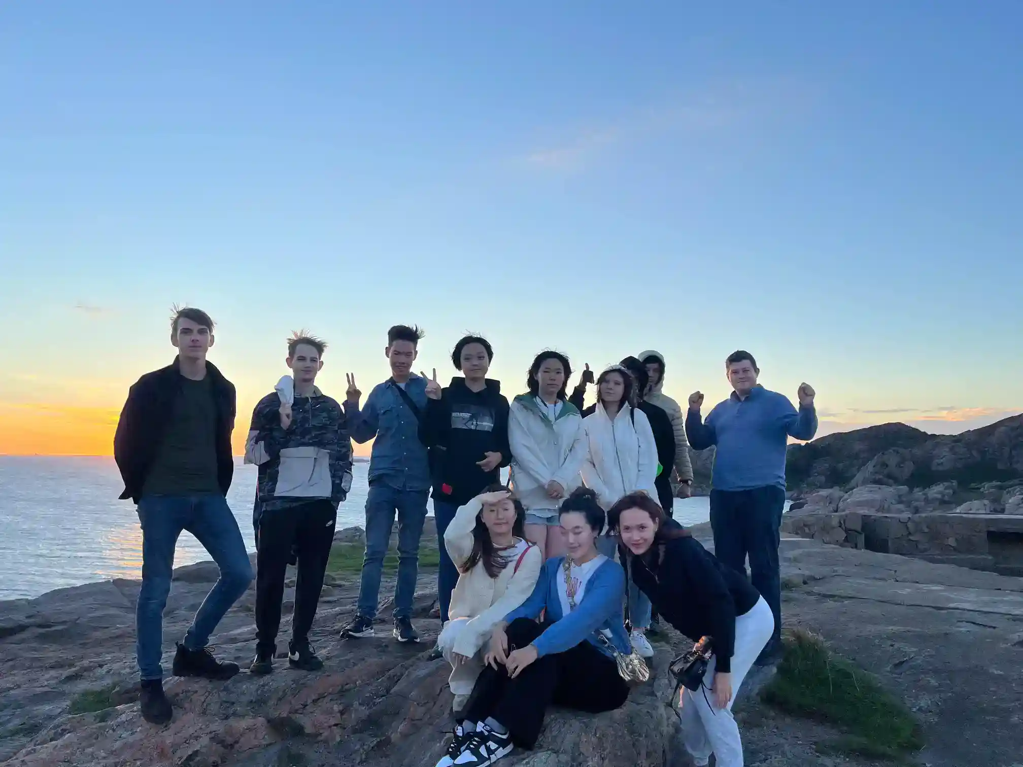 Students enjoying a scenic outdoor excursion during sunset at a rocky coast, fostering cultural exchange and global education.