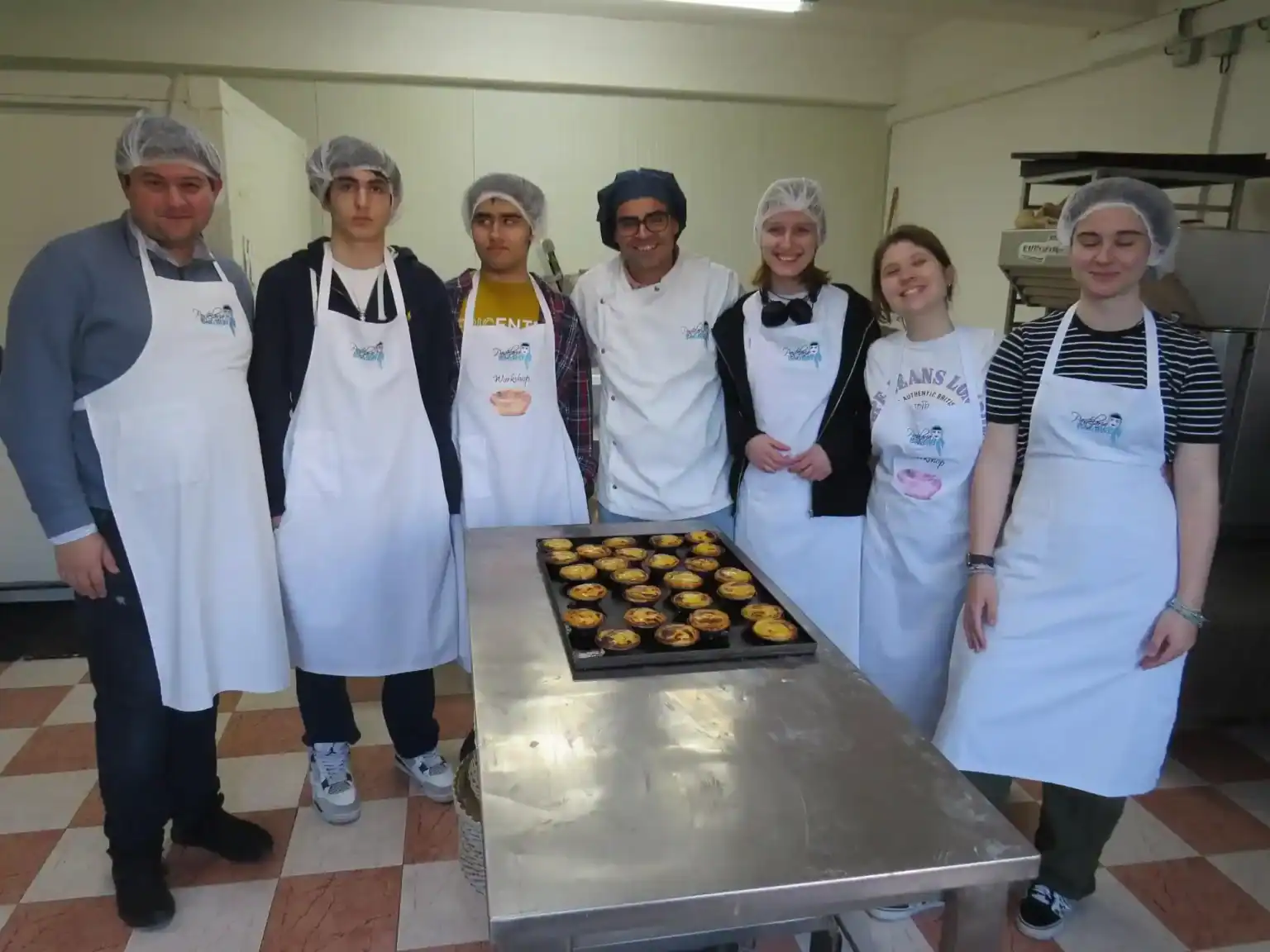 Students participating in a cooking workshop at a World Schools culinary program, wearing aprons and hairnets.