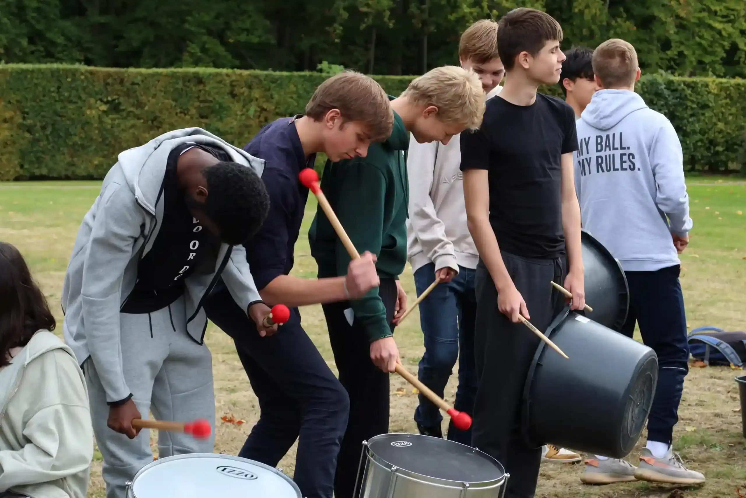 Students playing drums outdoors at a school campus schoolyard.