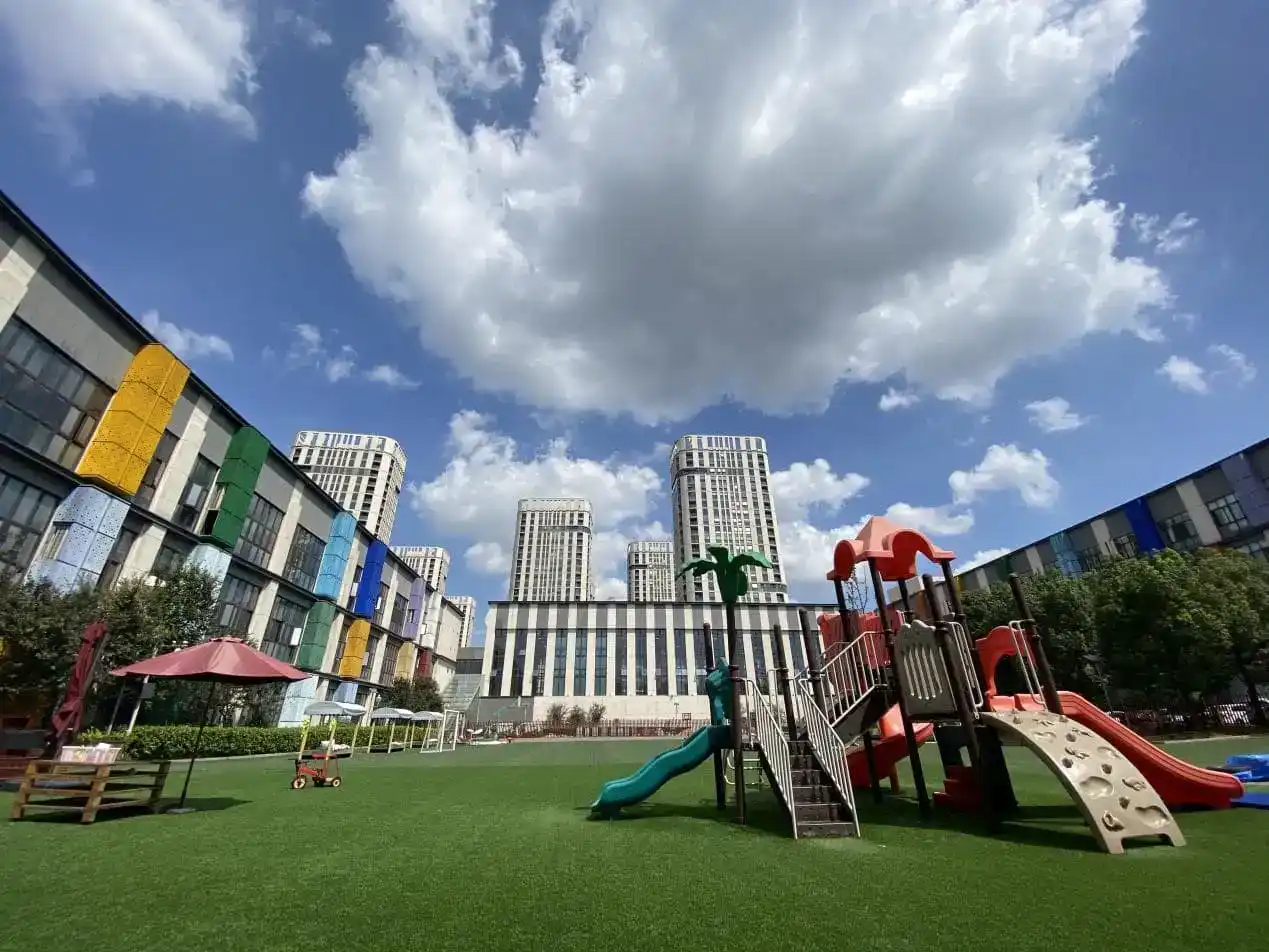 Bright outdoor playground at an international school with modern high-rise buildings in the background.