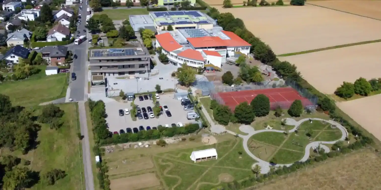 Modern international school with sports facilities, parking, and green outdoor areas in a suburban setting.