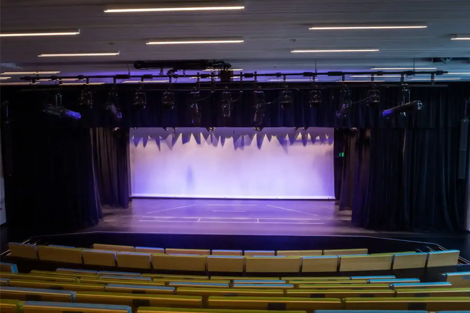Escenario de teatro luminoso con telones, ideal para representaciones escolares y concursos de talentos.