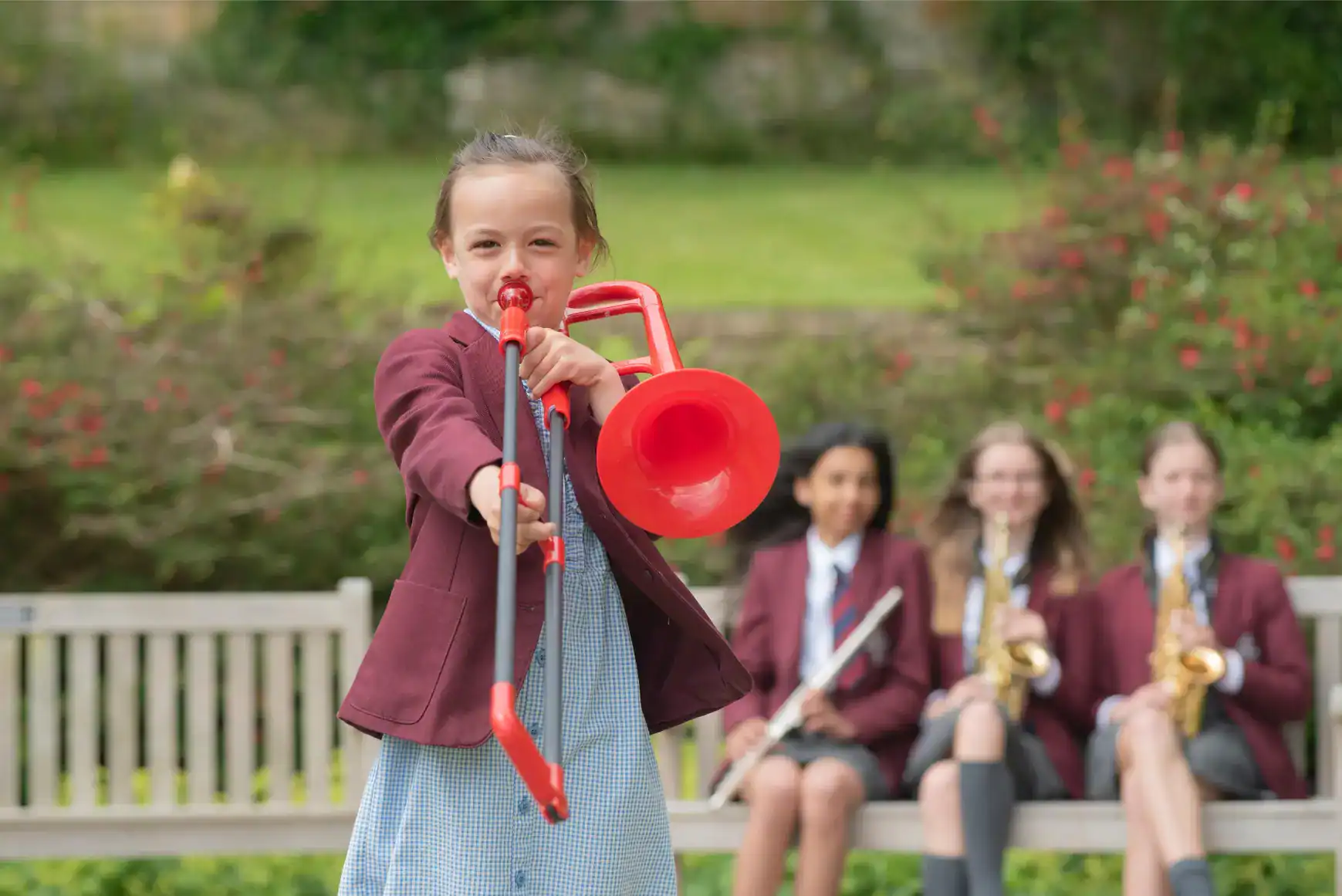 Ragazza brillante che suona la tromba all'aperto in una scuola con i compagni sullo sfondo, promuovendo l'eccellenza educativa e i programmi musicali.