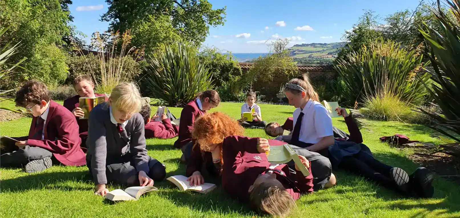 Giovani studenti che leggono all'aperto in un giardino lussureggiante, godendosi una tranquilla pausa educativa.