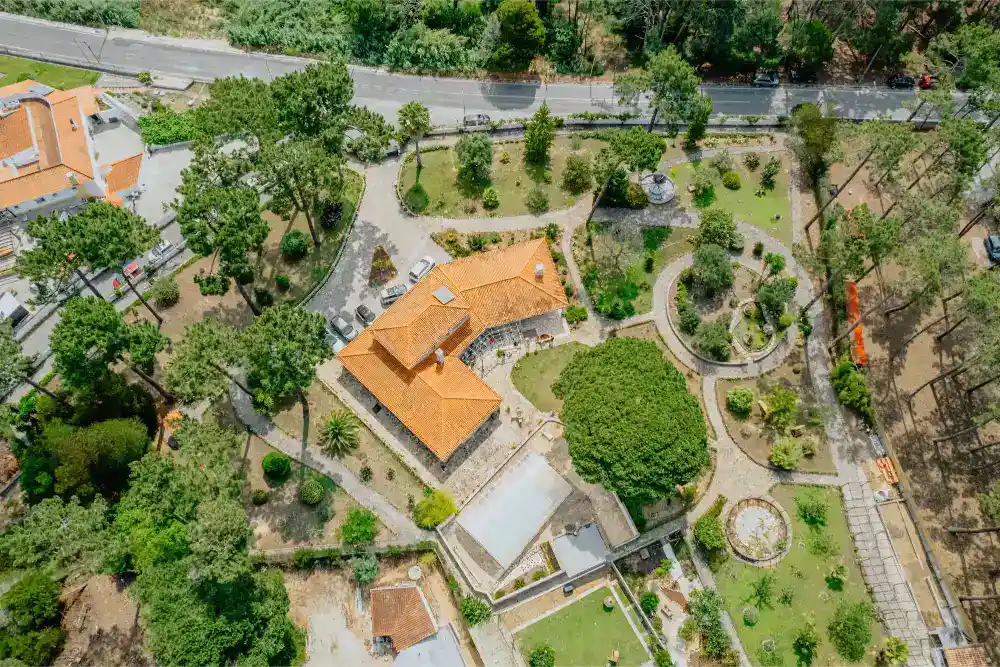 Lush green campus of a private school with gardens and walking paths, surrounded by trees and neighboring buildings.