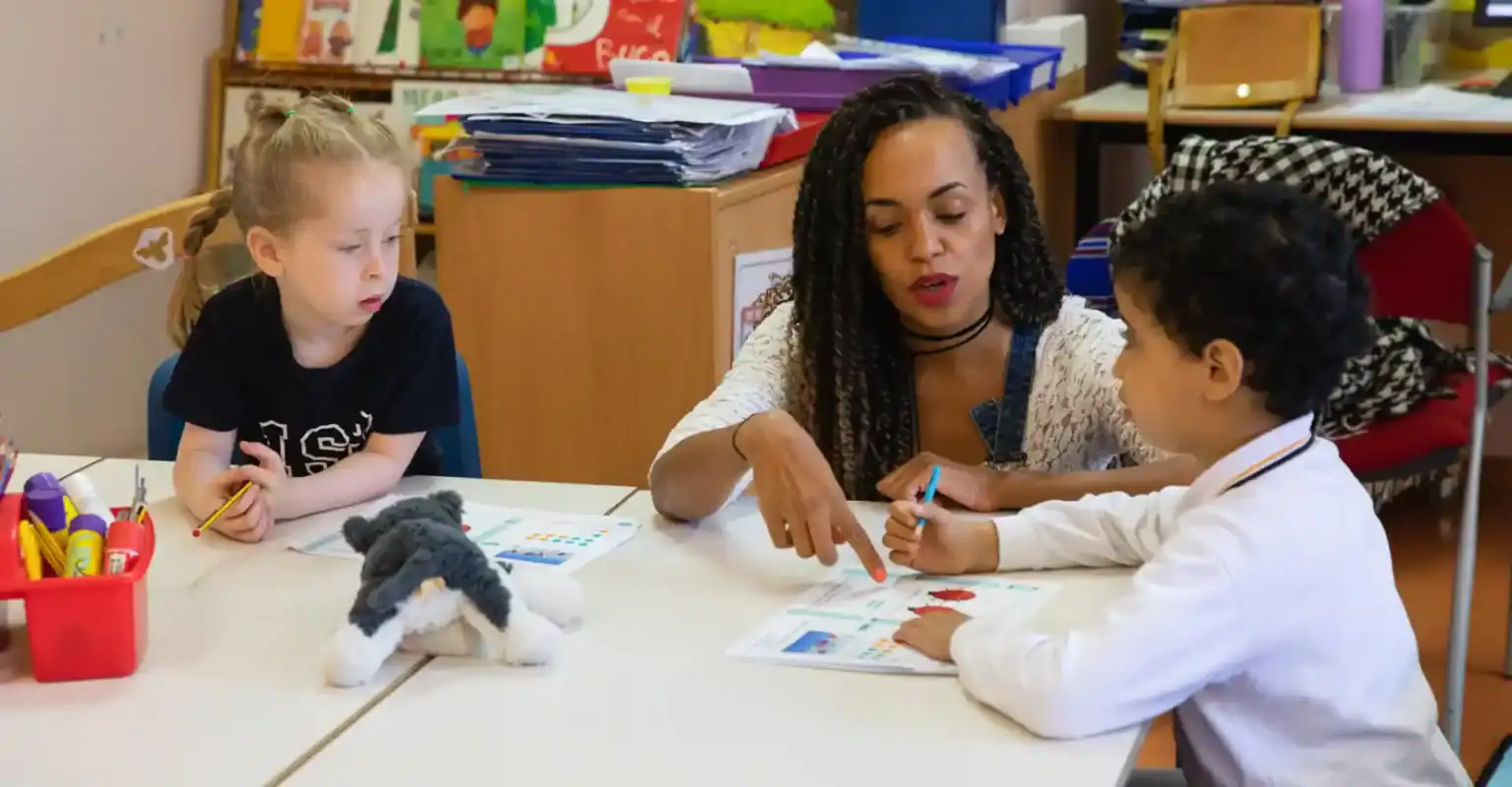 Engagierte Lehrerin, die jungen Schülern in einer Klasse mit Schwerpunkt auf internationaler Bildung hilft.