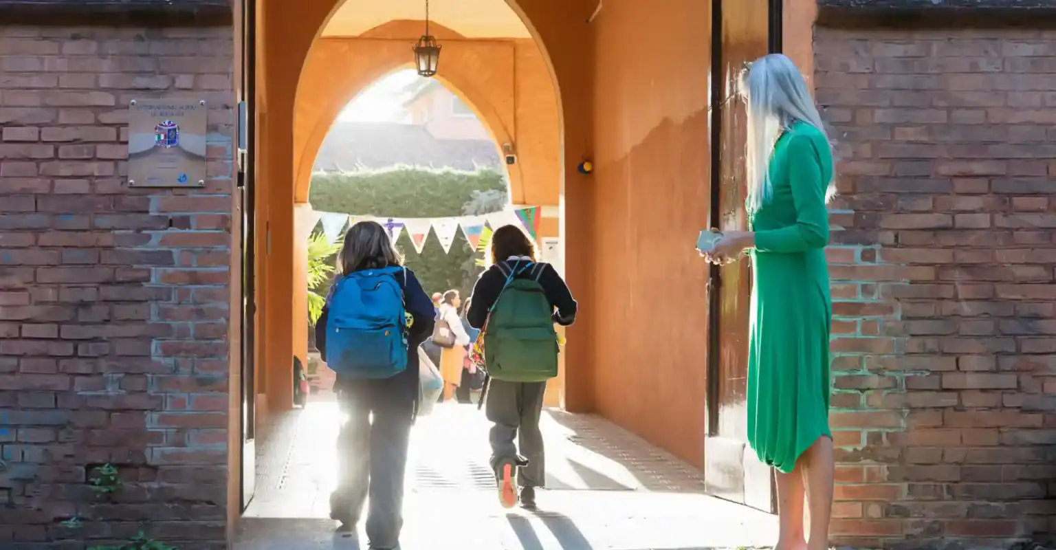 Aufgeweckte Schüler betreten eine angesehene internationale Schule durch einen warmen, einladenden Torbogen mit bunten Bannern und üppigem Grün.