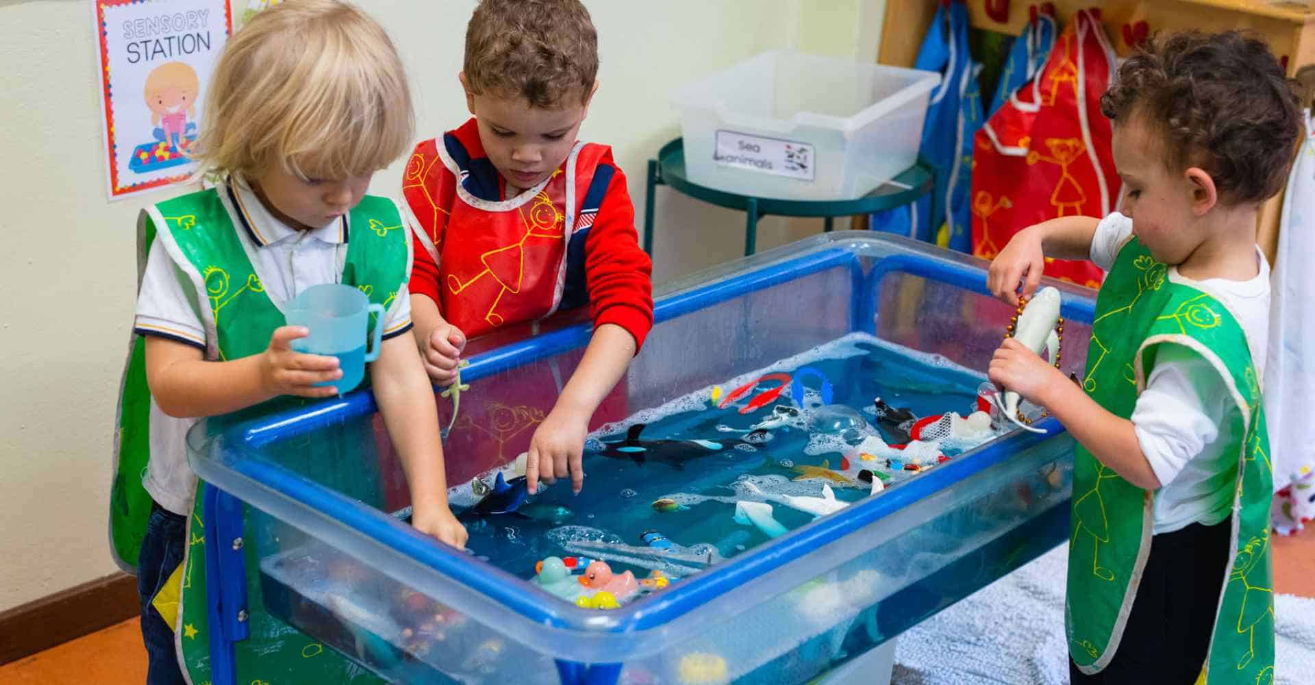 Bunte Kinder, die sich mit der Wasserstation beschäftigen, sensorisches Spiel, Kindergartenaktivität, frühkindliche Bildung, Lernen durch Spielen.