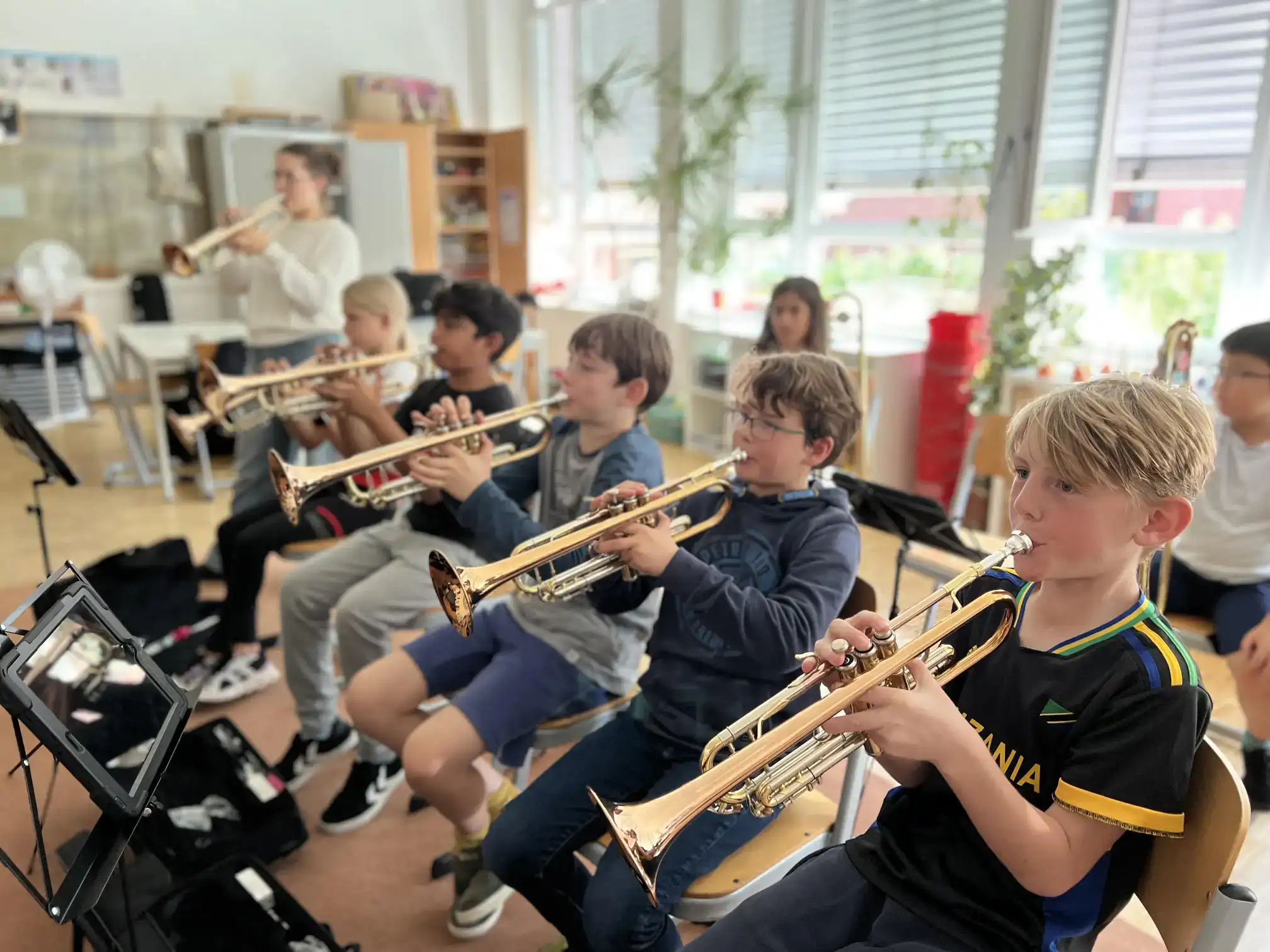 Young students playing trumpets in a classroom, learning music at an international school.