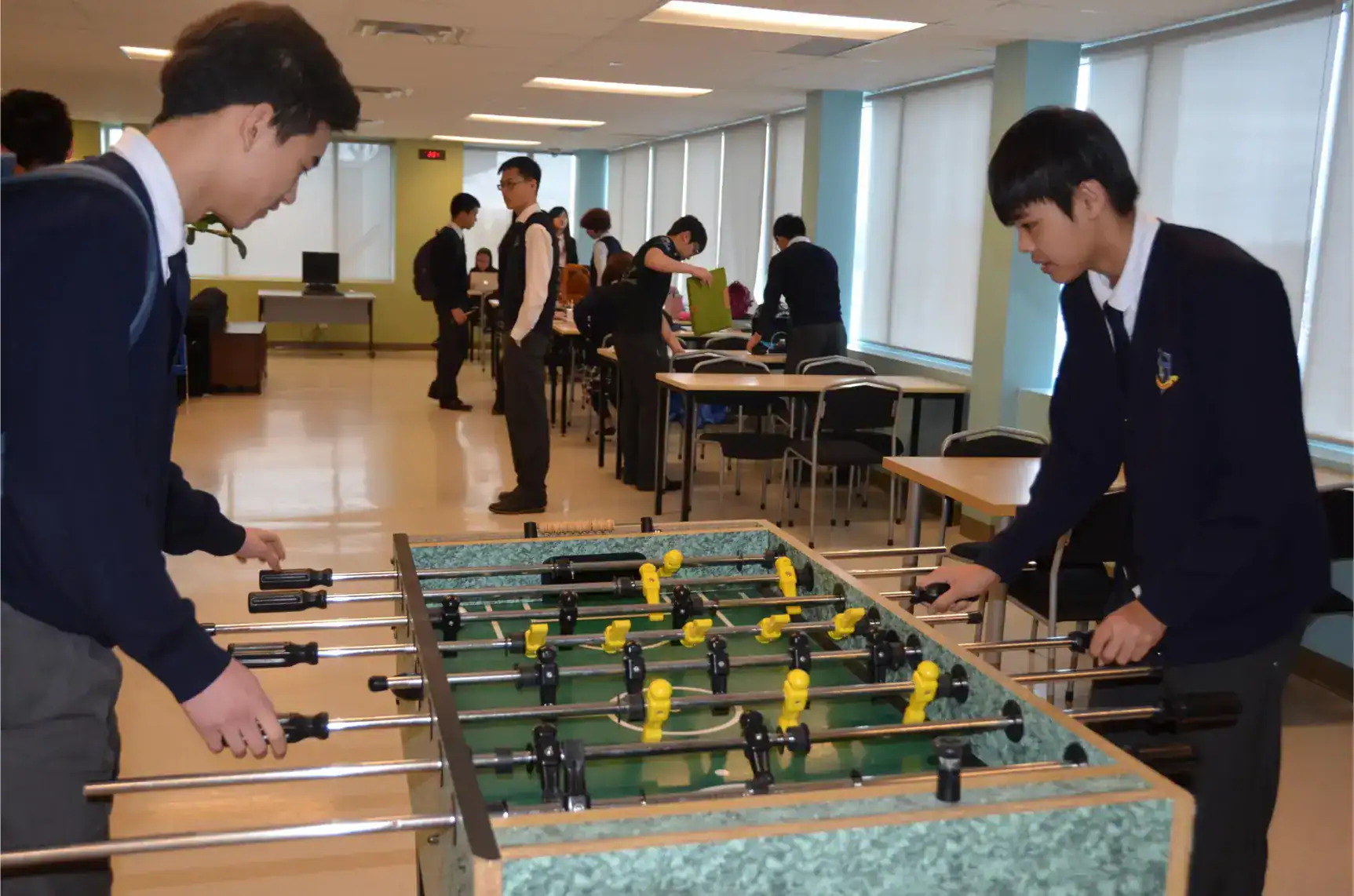 Young students playing foosball in a modern, international school classroom.