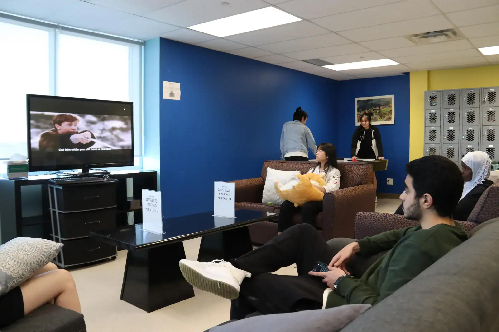 Comfortable waiting area in an international school lounge, featuring students watching TV and socializing.