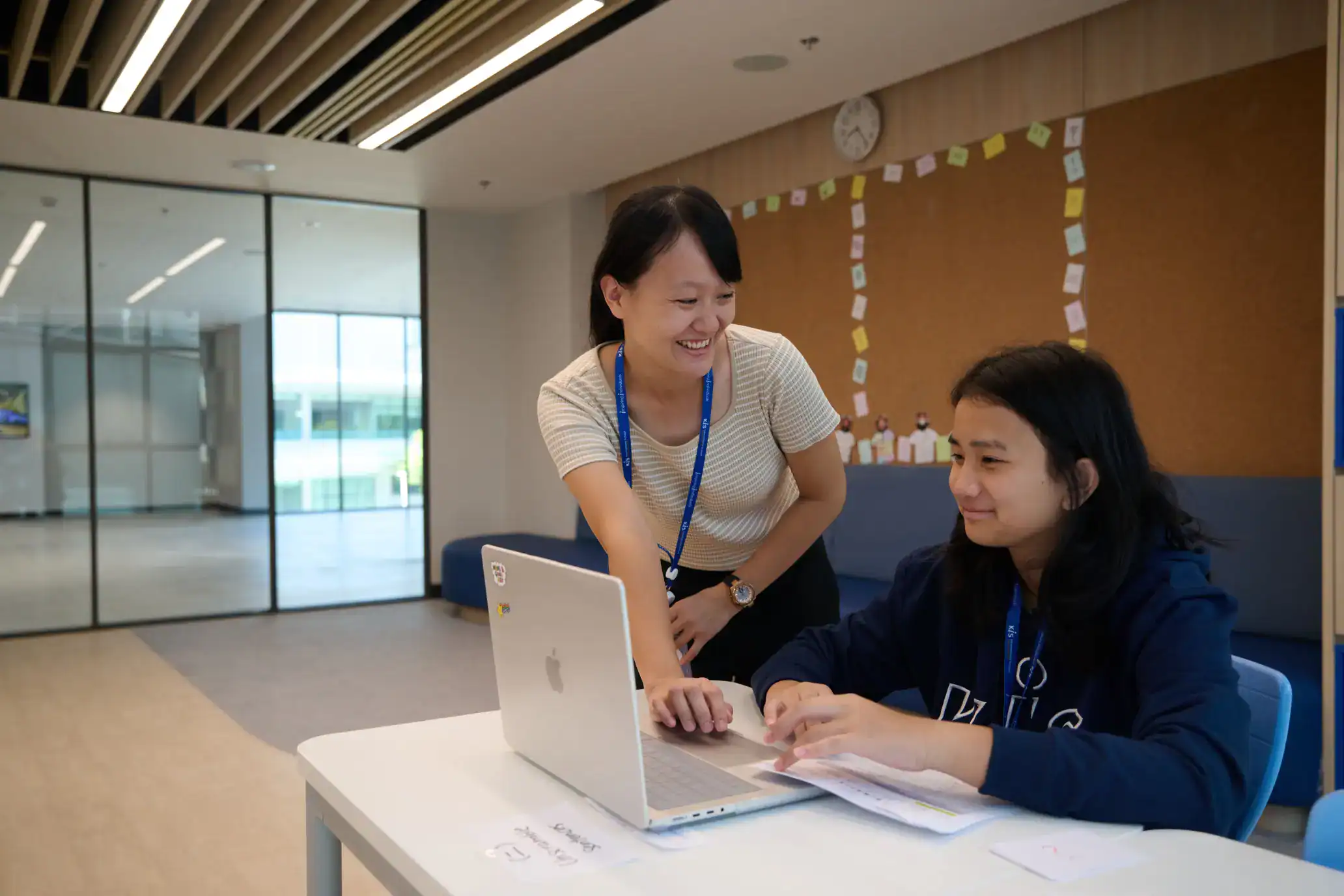 Engaged teacher assisting student with laptop in a modern school environment.