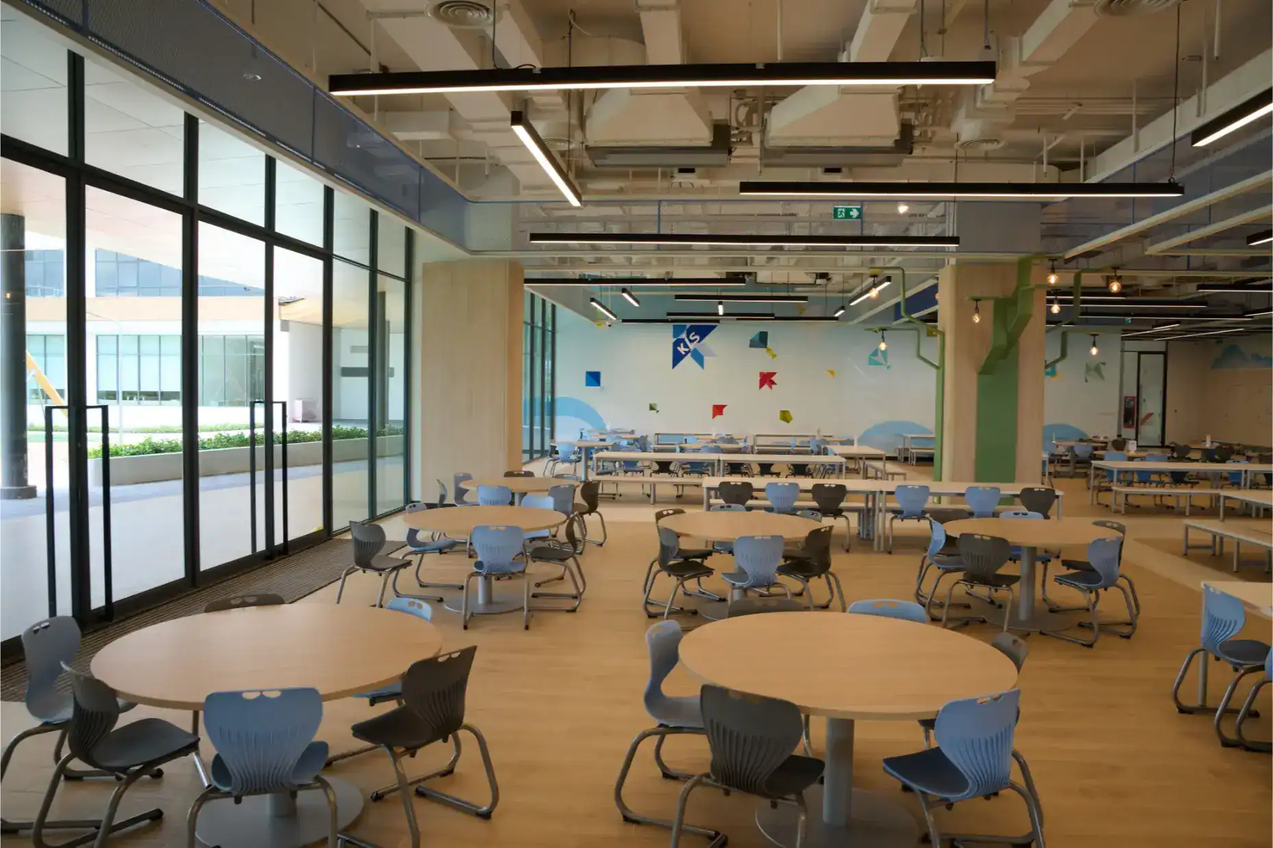 Modern indoor school cafeteria with round tables and colorful wall art, bright natural lighting, and a contemporary design.