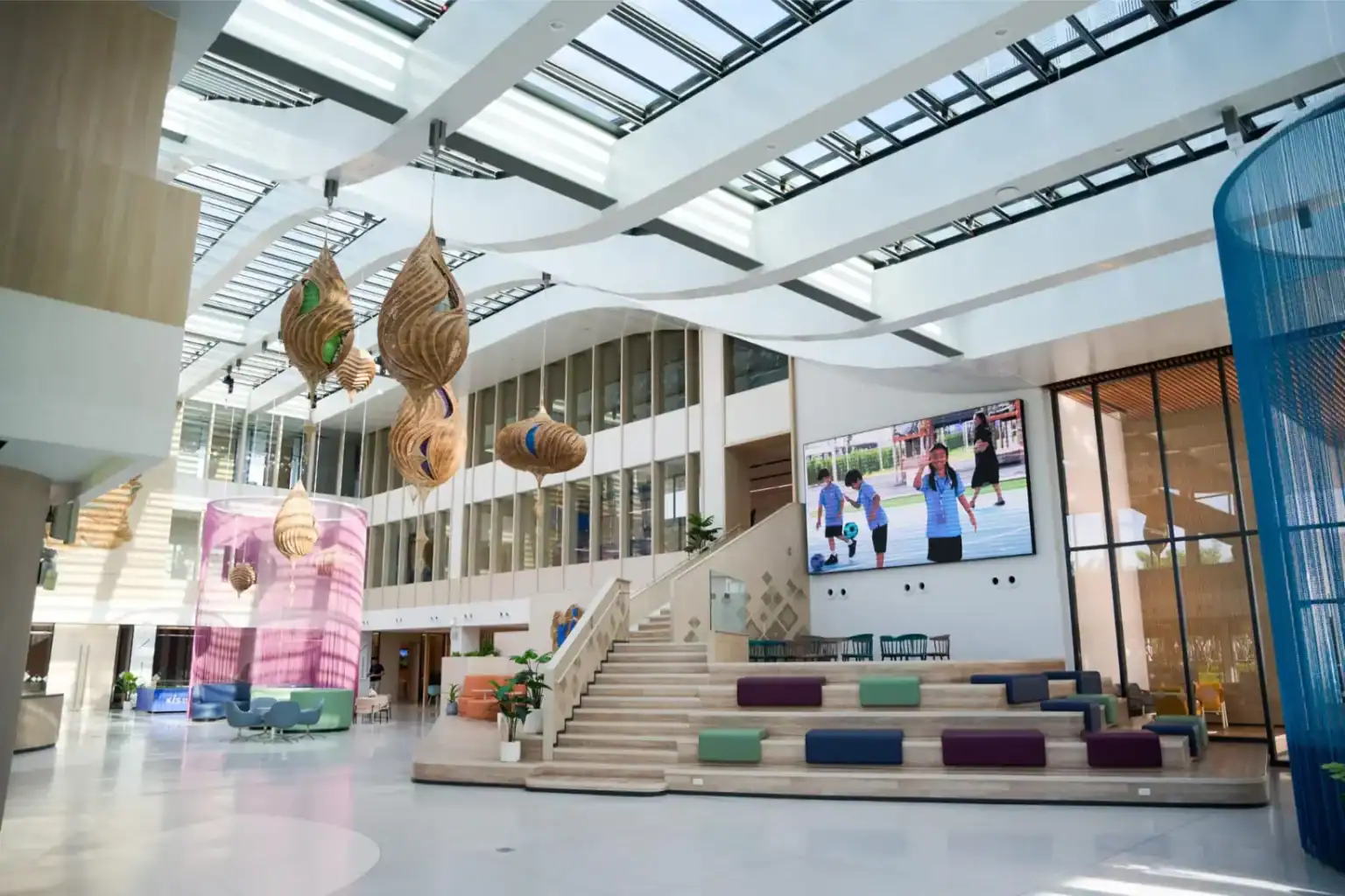 Modern school lobby with contemporary interior design, colorful seating, and large digital screen featuring students.