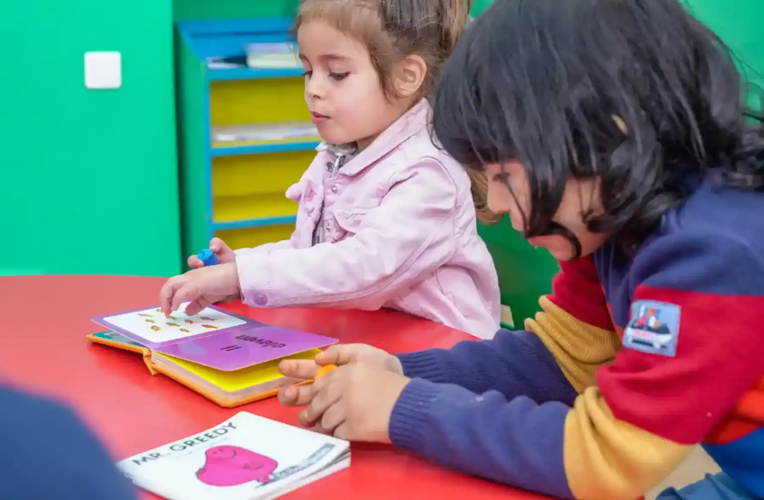 Young children engaged in educational reading activity at a colorful classroom.