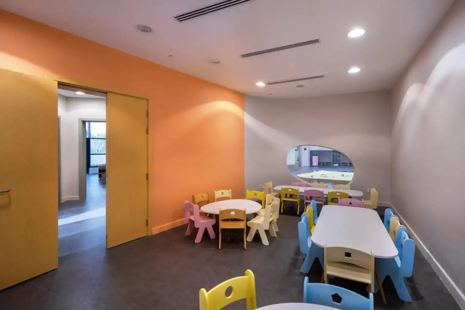 Bright indoor preschool classroom with colorful chairs and tables for young children.