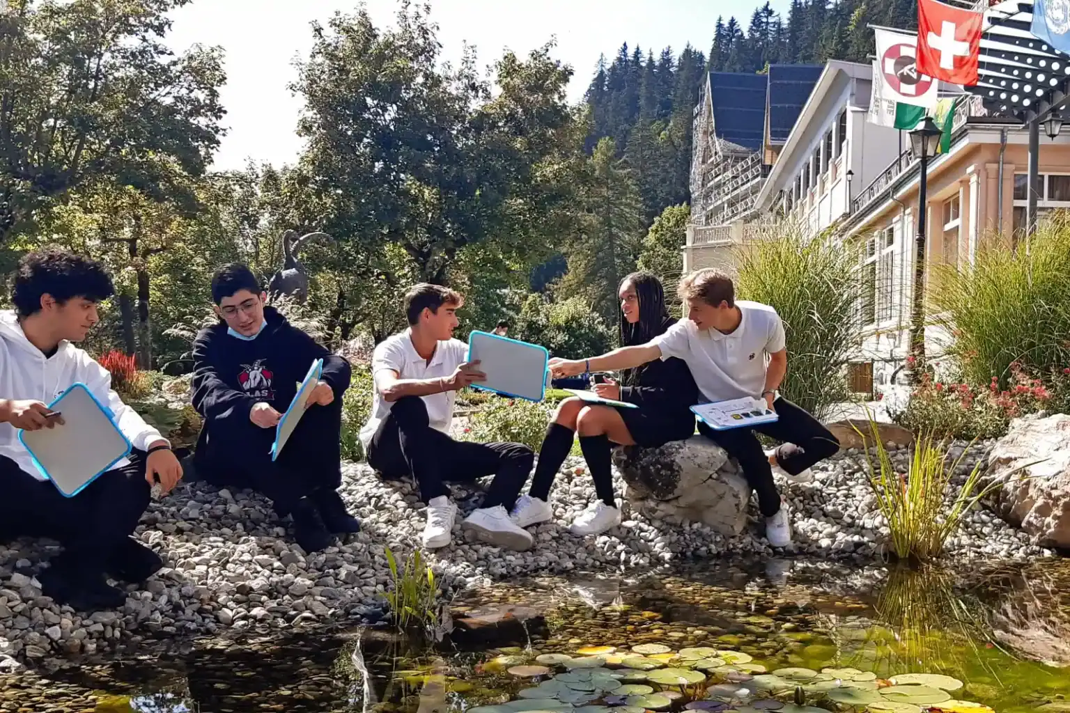 Students studying outdoors at a scenic school campus with greenery and building views.