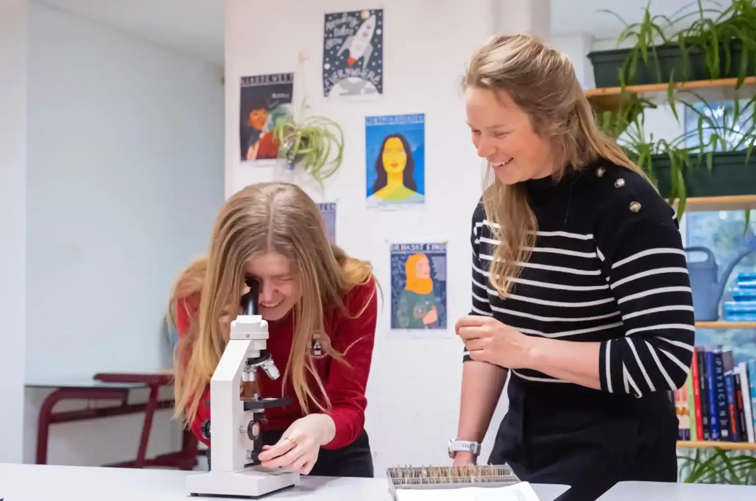 Young female student with microscope and teacher engaging in science experiment at school.