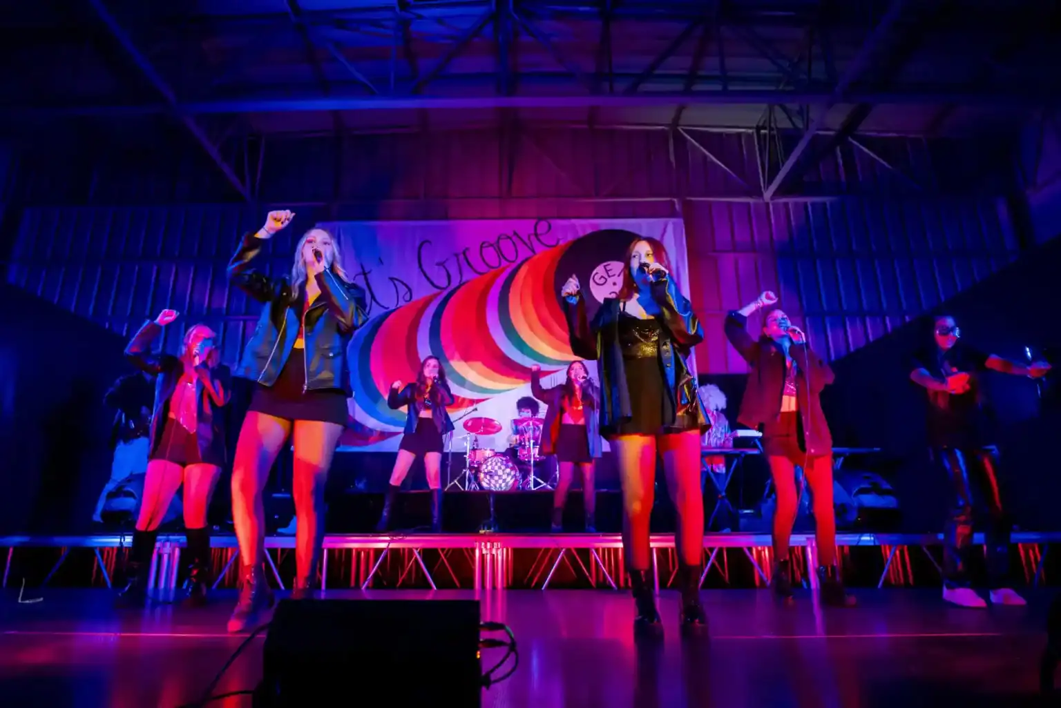 ワールドスクールのイベントで、カラフルな背景のステージで躍動する少女たちのミュージカル・パフォーマンス。.